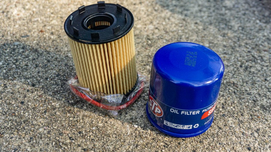 A yellow cartridge oil filter next to a blue spin-on oil filter on the ground