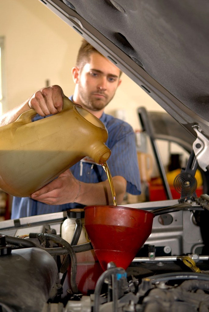 A mechanic pours oil into a car engine as part of regular maintenance, which can improve gas mileage
