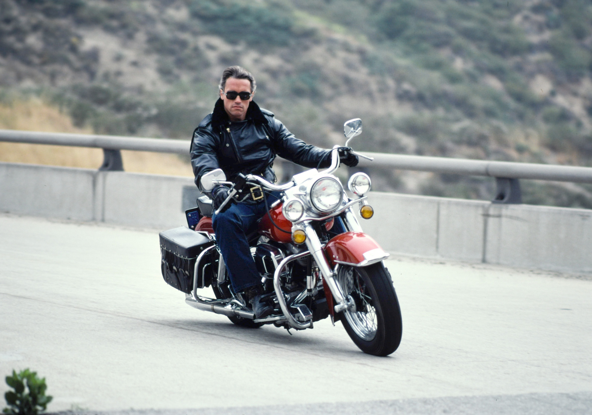 Arnold Schwarzenegger going around a corner faster on a motorcycle.