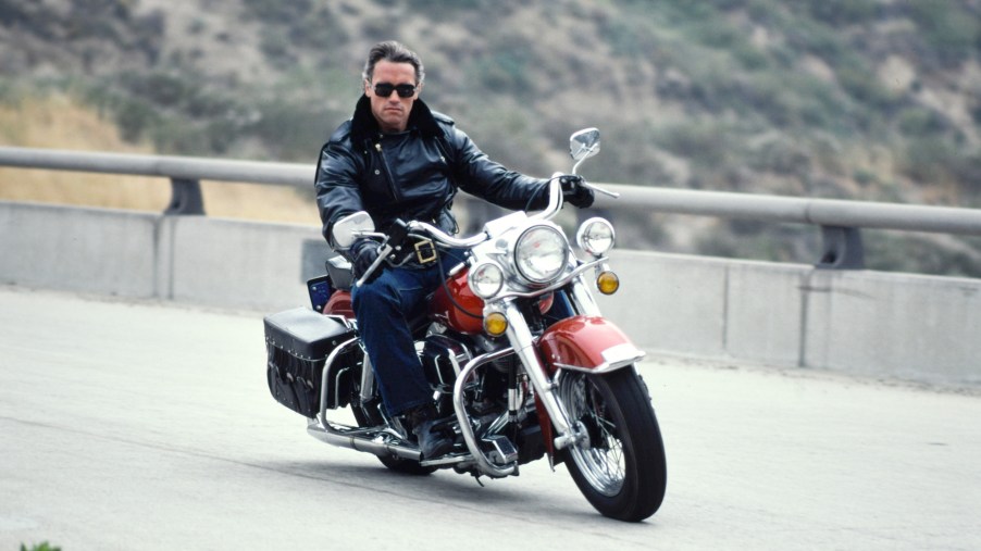 Arnold Schwarzenegger going around a corner faster on a motorcycle.