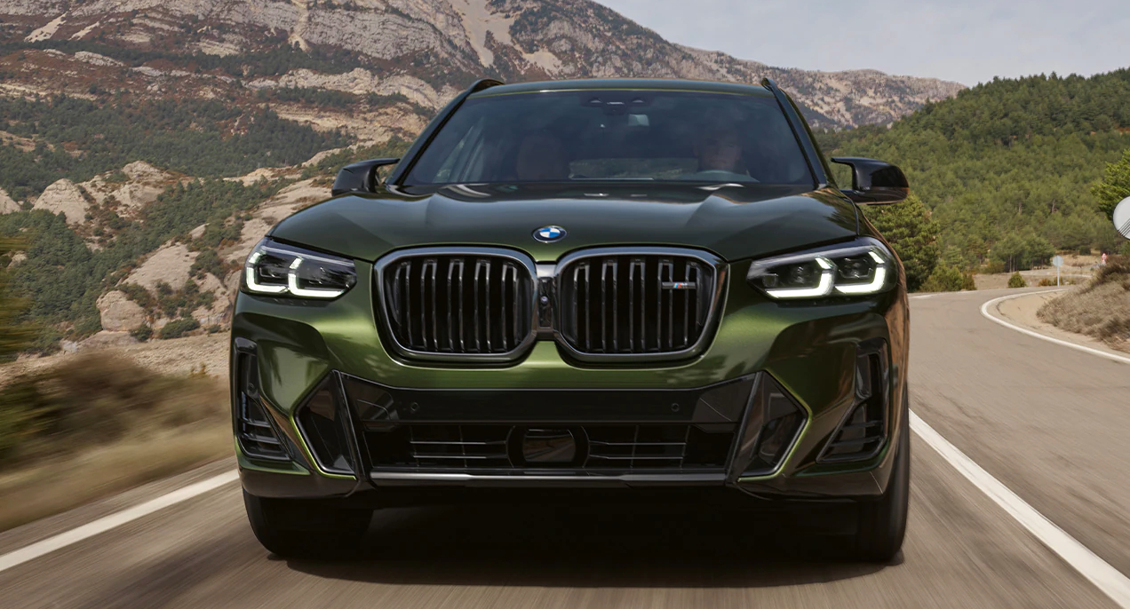 A green BMW X3 luxury compact SUV is driving on the road.