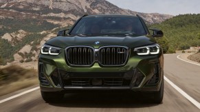 A green BMW X3 luxury compact SUV is driving on the road.
