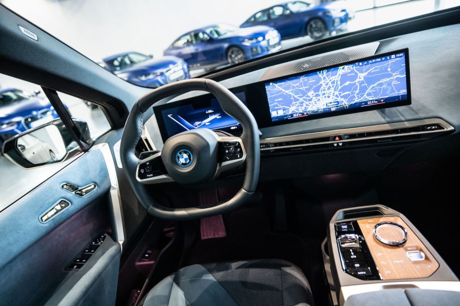 The cockpit of a BMW iX with a two-spoke steering wheel and large displays.