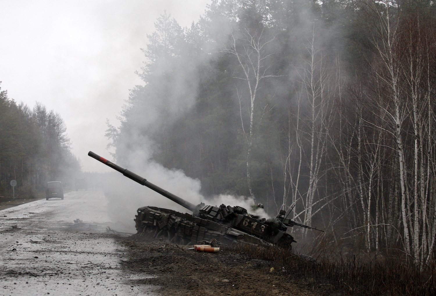 Russian tank burning by the side of a Ukrainian road, birch trees visible in the background.