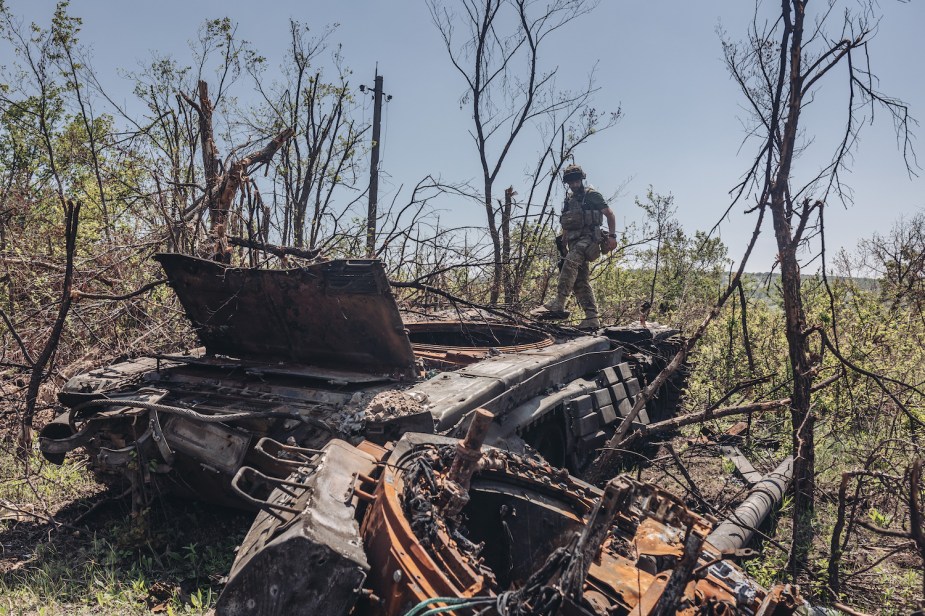 Ukrainian soldier standing on the burnt husk of a Russian tank in the middle of the woods.