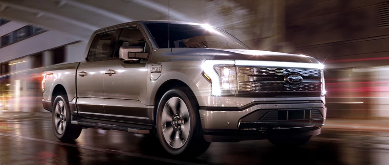 A gray 2022 Ford F-150 Lightning is driving on the road.
