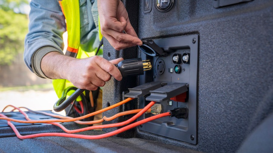 Promo shot of a construction worker's hands plugging a 220-volt cable into the Ford F-150 PowerBoost's Pro Power inverter.