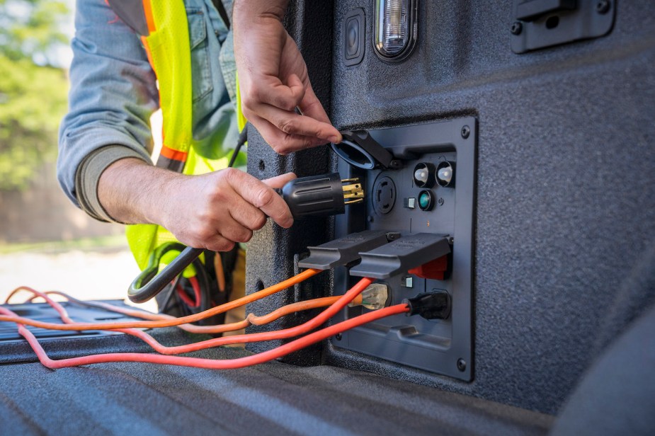 Promo shot of a construction worker's hands plugging a 220-volt cable into the Ford F-150 PowerBoost's Pro Power inverter.