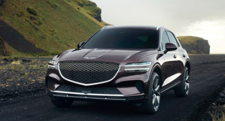 A gray 2022 Genesis GV70 luxury compact SUV is driving on the road. 