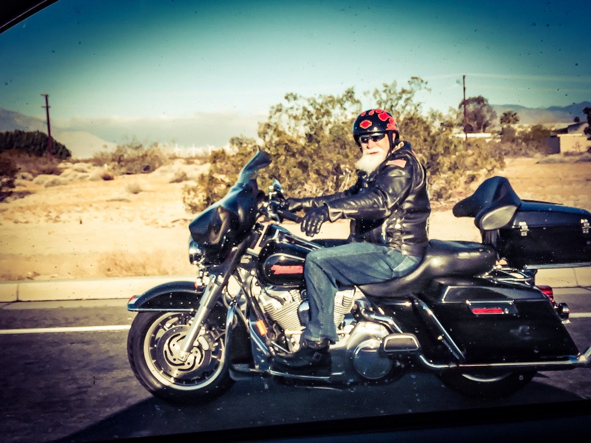 A motorcyclist on a Harley wearing a jacket, carnations and helmet in California. 