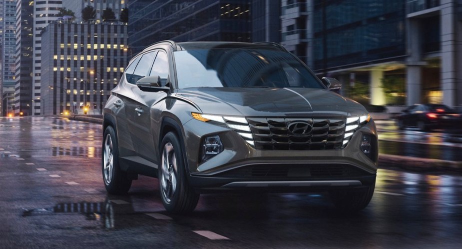 A gray 2022 Hyundai Tucson compact SUV is driving on a wet road. 