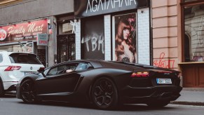 The rear 3/4 view of a matte-black-painted Lamborghini Aventador on a city street