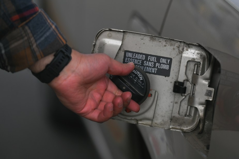 A gas station customer removes their car's gas cap before filling the tank