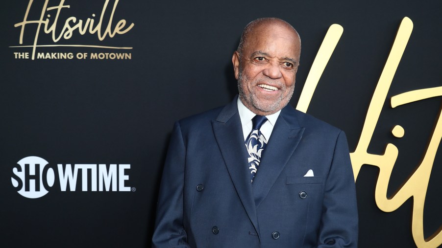 Motown's Berry Gordy dressed in a suit in front of a black and gold front.