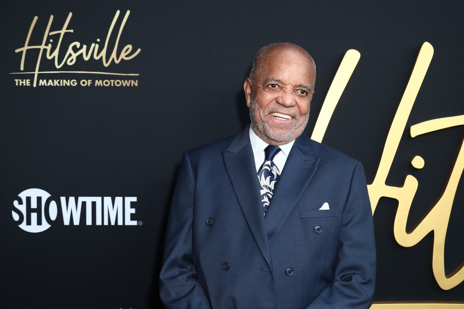 Motown's Berry Gordy dressed in a suit in front of a black and gold front.
