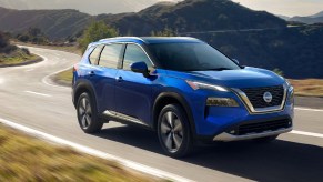 A blue 2022 Nissan Rogue small SUV is driving on the road.