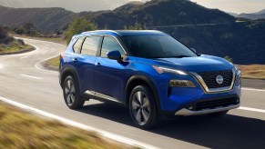 A blue 2022 Nissan Rogue small SUV is driving on the road.