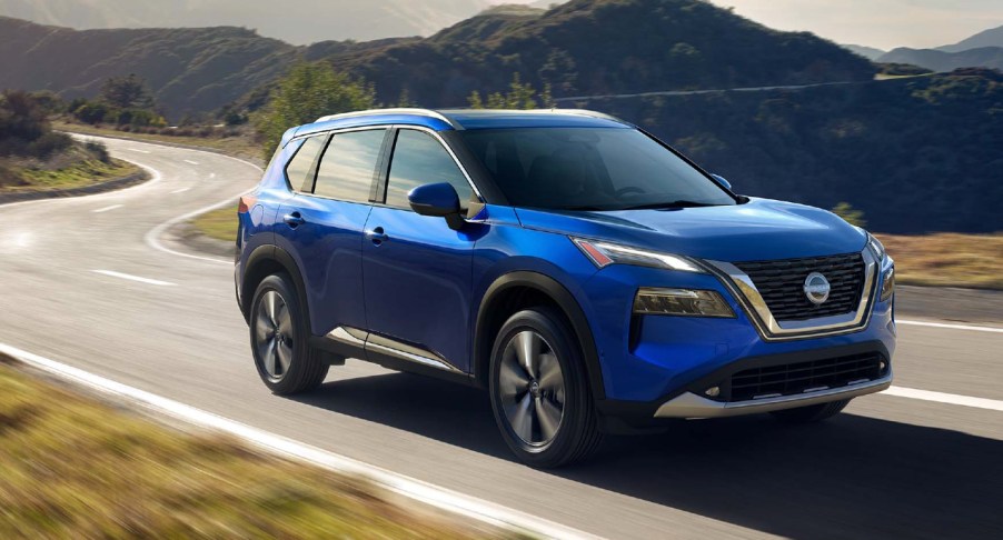 A blue 2022 Nissan Rogue small SUV is driving on the road.