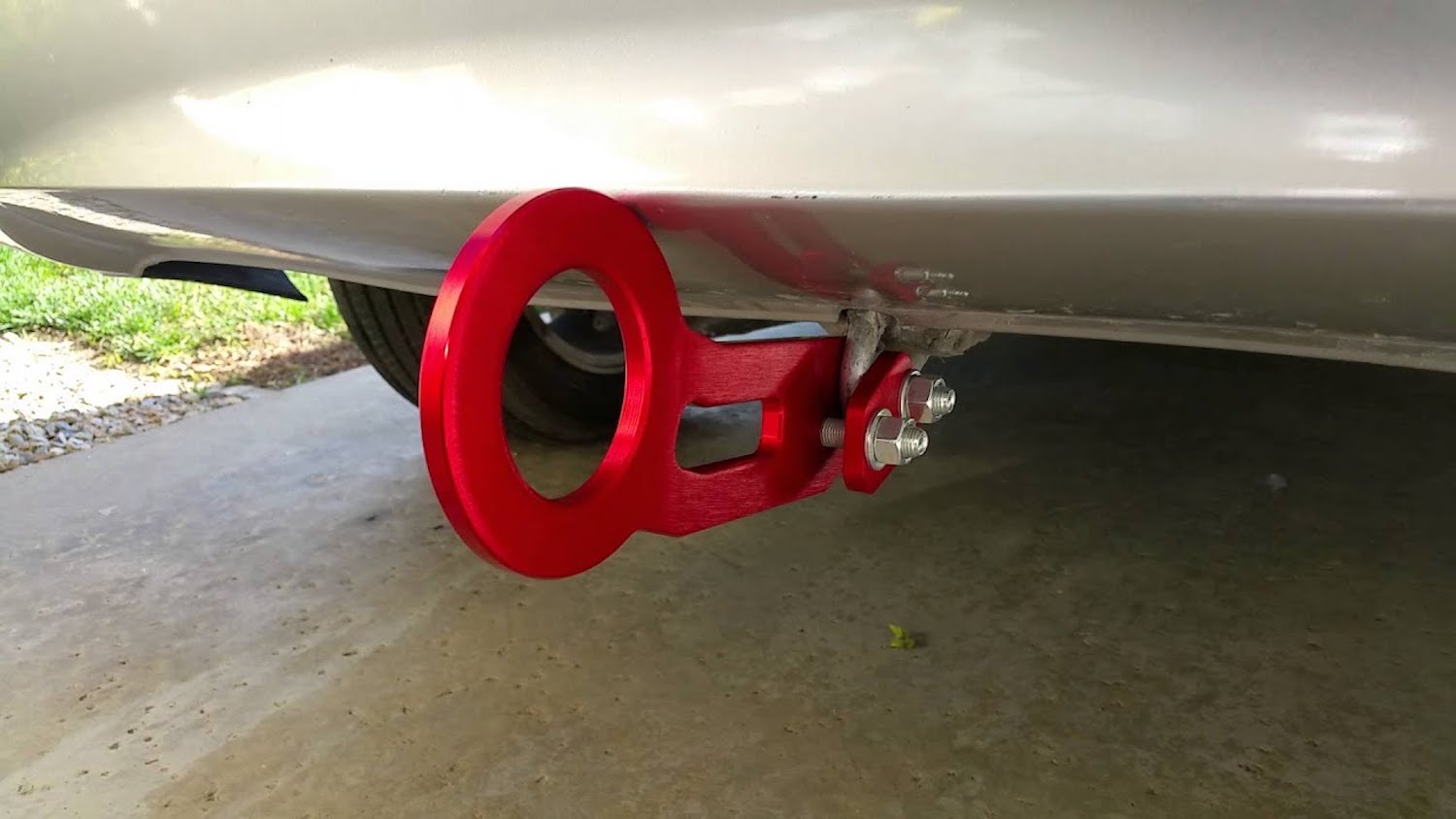 Closeup of a red aftermarket JDM tow hook installed under the rear bumper of a car.