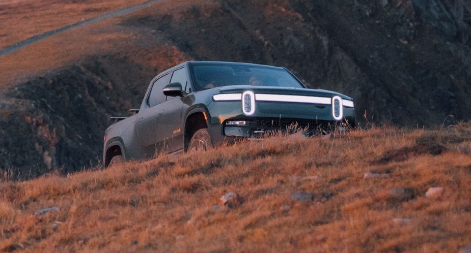 A green Rivian R1T is parked on a hill. 