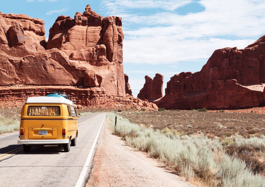 Yellow volkswagen bus on a road trip through the desert, on a road winding between red rock formations.