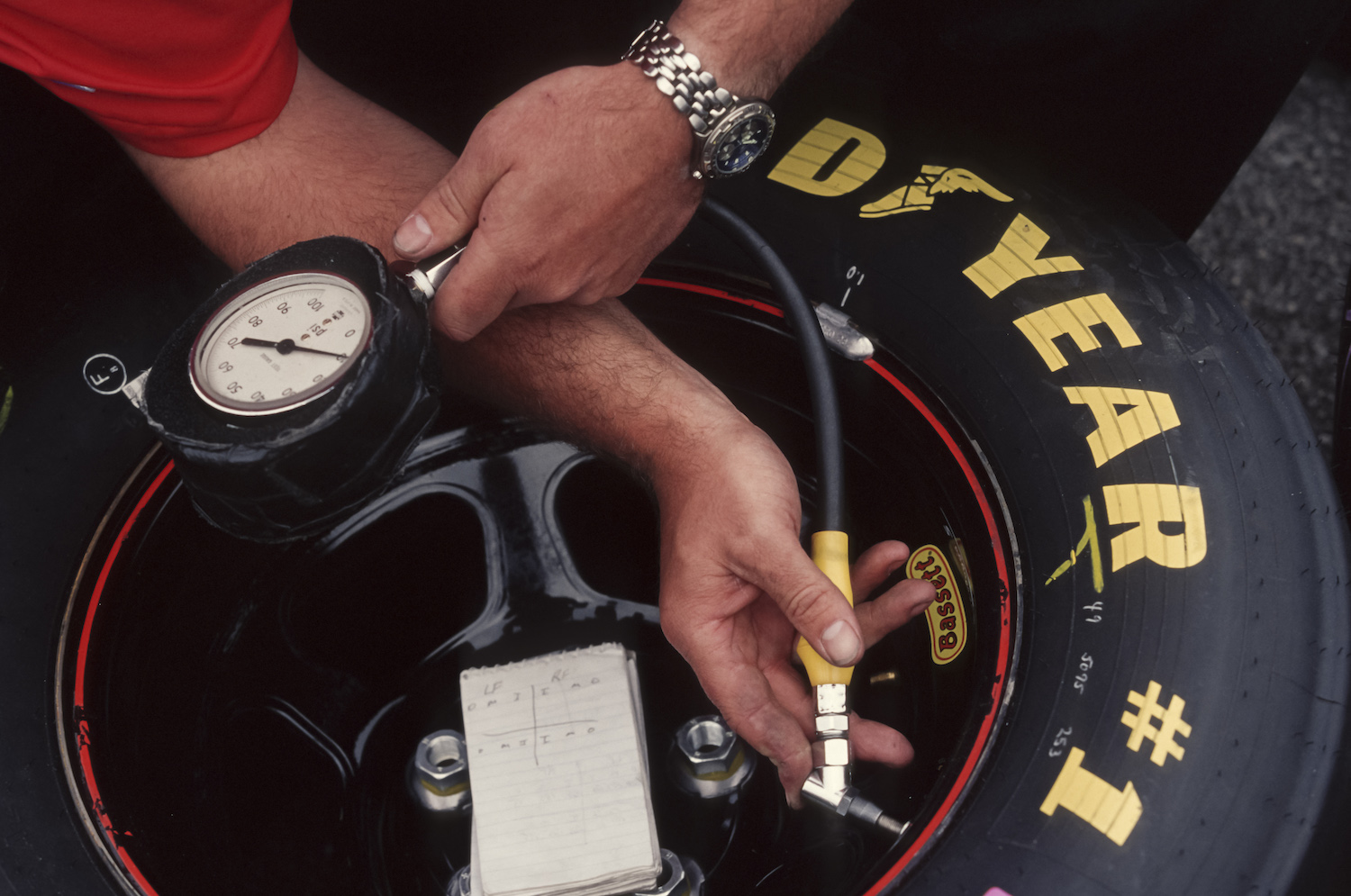 The hands of a NASCAR technician checking the psi of a Good Year racing tire with an air pressure gauge.