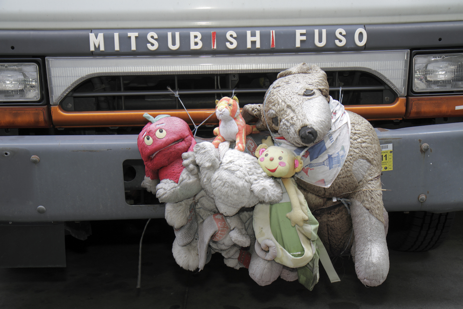 A stack of stuffed animals decorating the front bumper of a MIstubishi Fuso. 