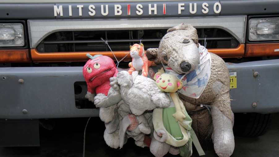 A stack of stuffed animals decorating the front bumper of a MIstubishi Fuso.