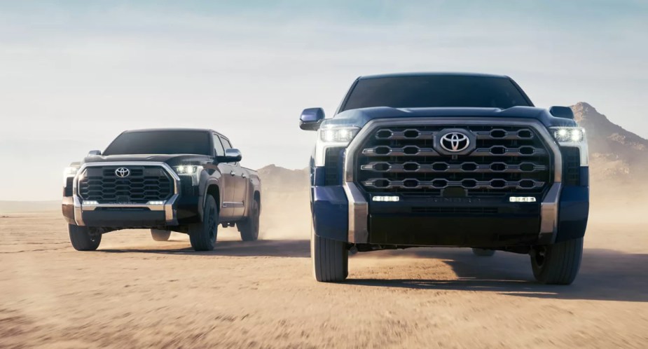 A black (L) and blue (R) 2022 Toyota Tundra are driving off-road. 