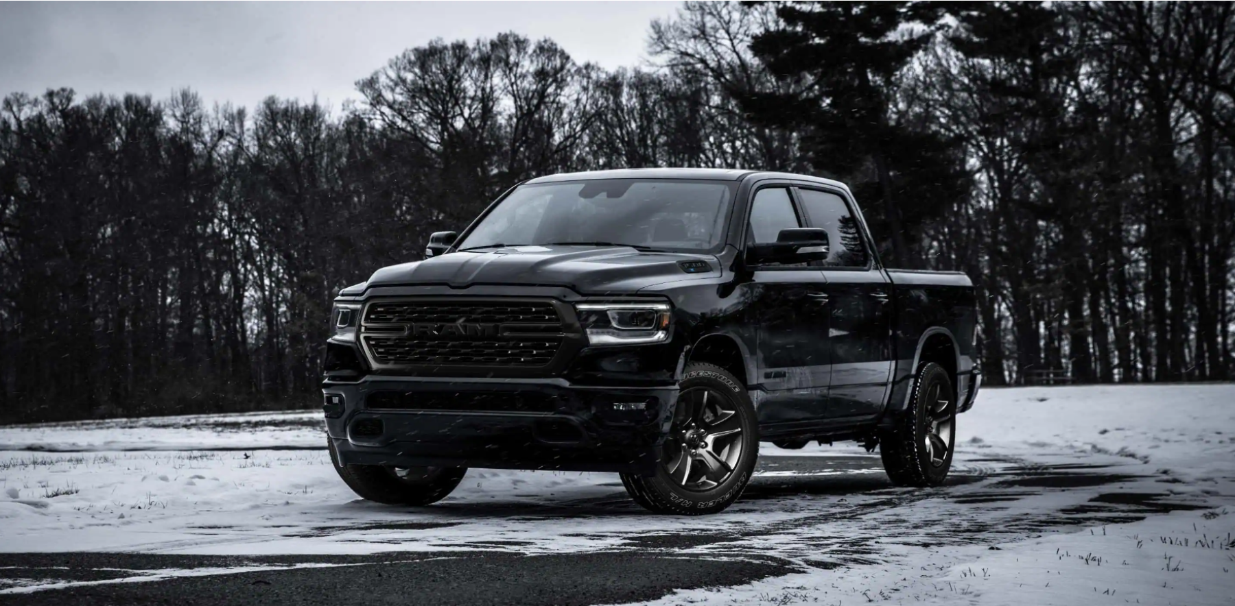 A black 2022 Ram 1500 full-size pickup truck parked on grass covered snow near barren trees