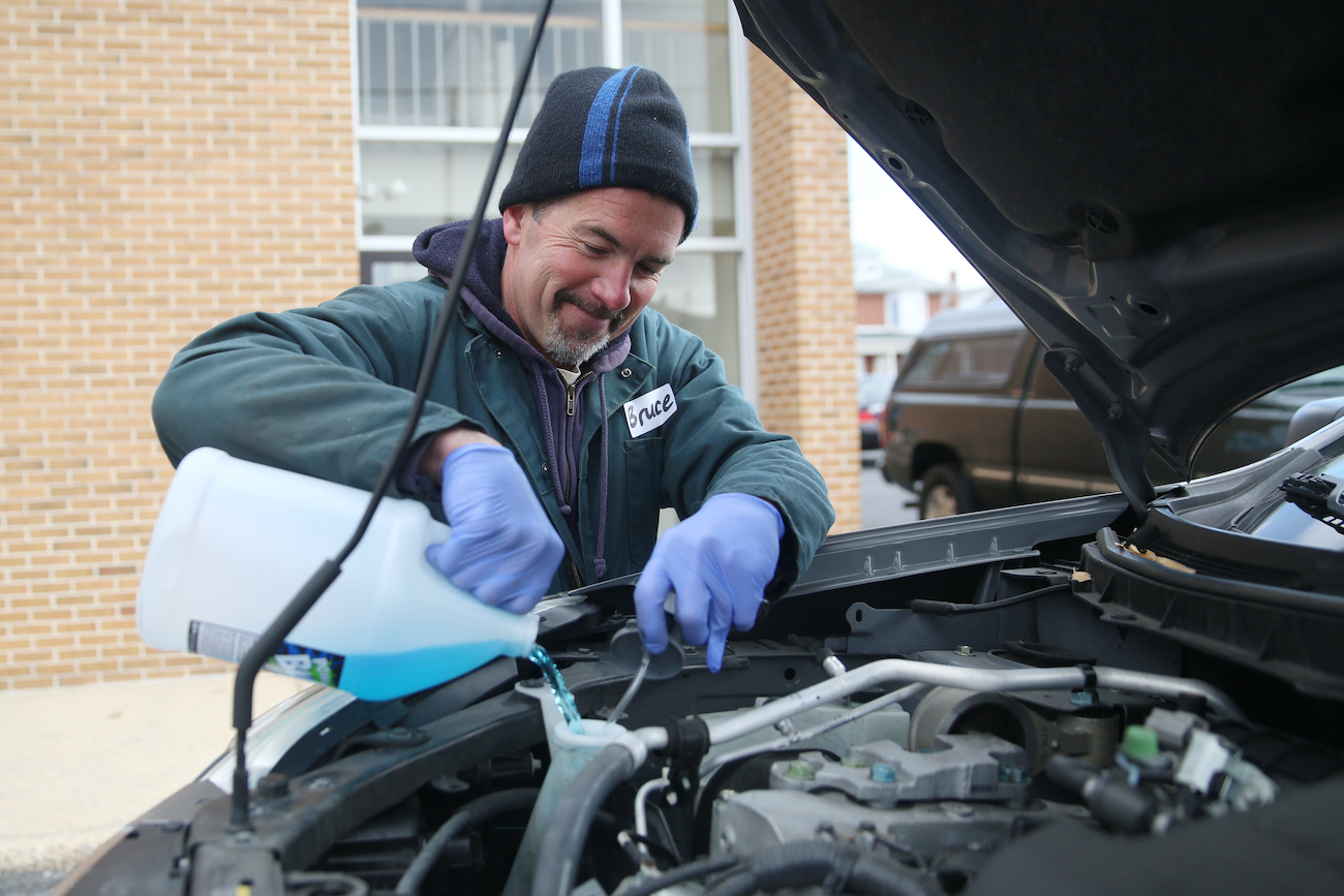 A mechanic pours coolant into a car