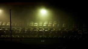 Rows of full-size pickup trucks parked under street lamps at a dealership, after dark.