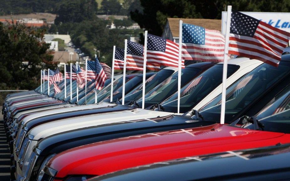A row of full-size pickup trucks for sale at a dealership, decorated with American flags.