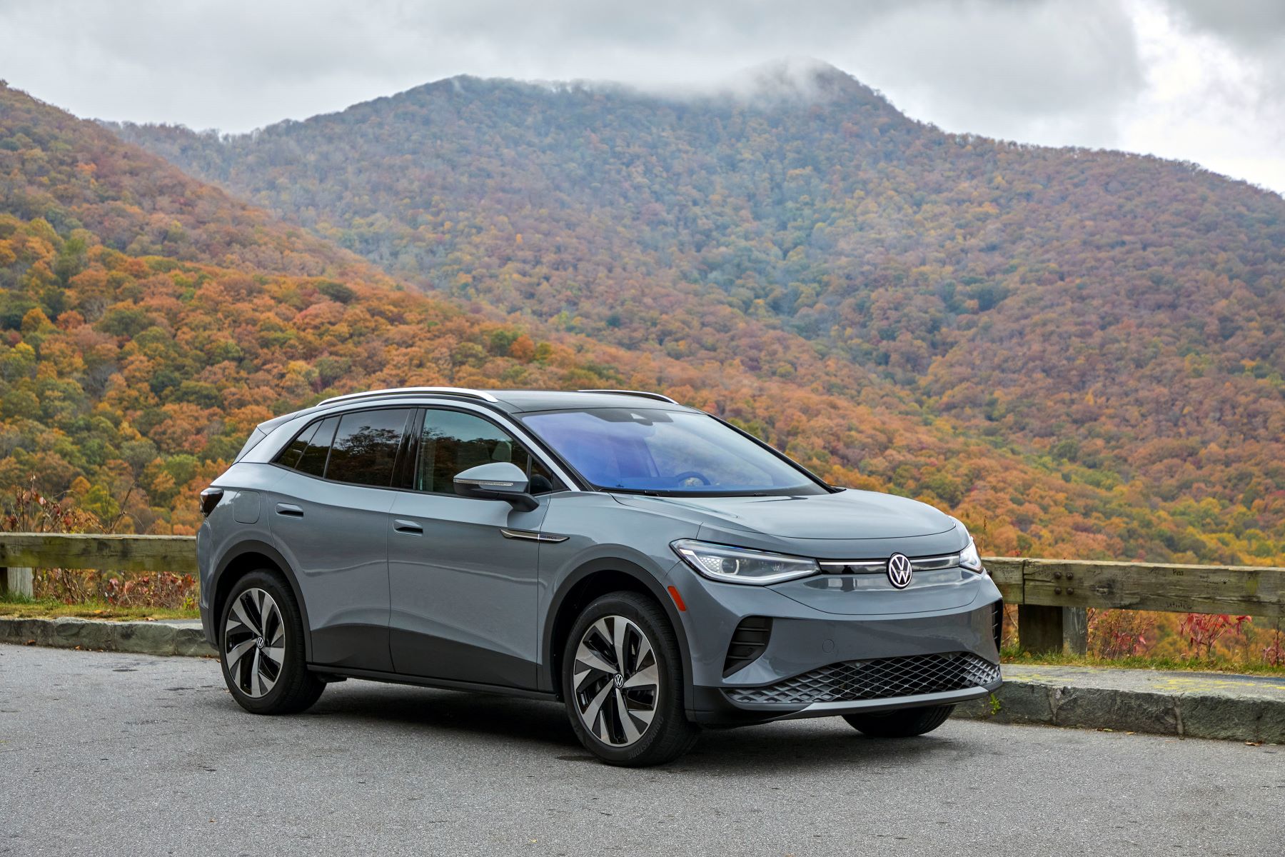 A gray 2021 Volkswagen ID.4 all-electric compact SUV model parked near a wooden fence near a foggy fall forest hill