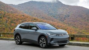 A gray 2021 Volkswagen ID.4 all-electric compact SUV model parked near a wooden fence near a foggy fall forest hill