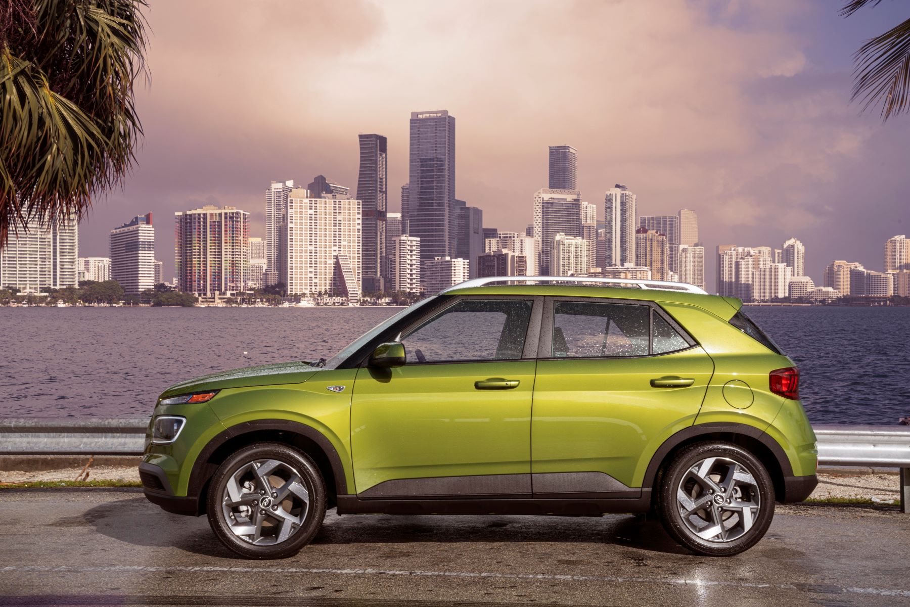 A sideshot of a green 2022 Hyundai Venue subcompact SUV model parked by the water with a skyline background