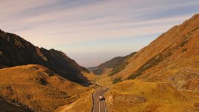A Jeep winding through a high altitude pass, the sky and mountains visible in the background.