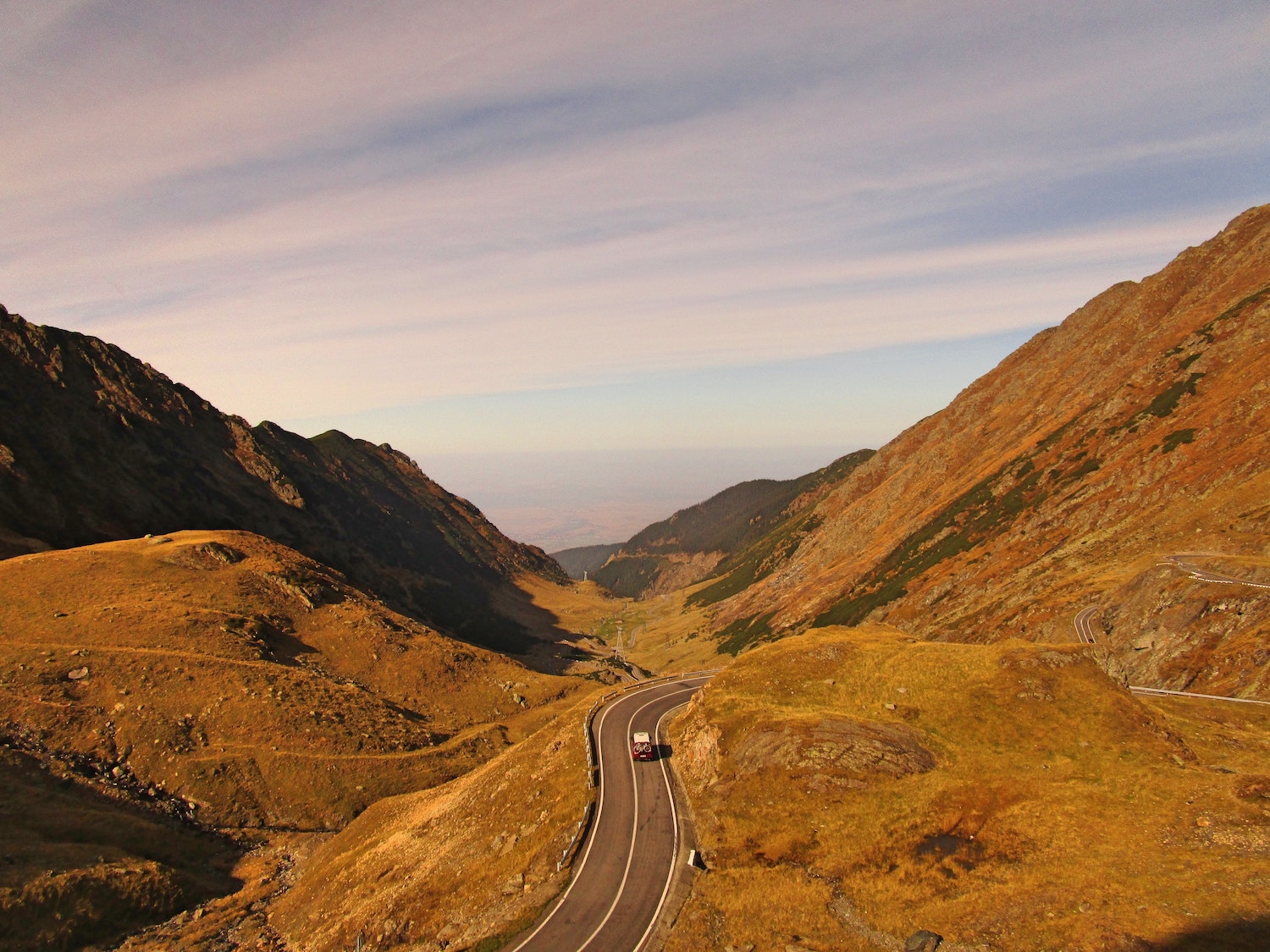 A Jeep winding through a high altitude pass, the sky and mountains visible in the background.