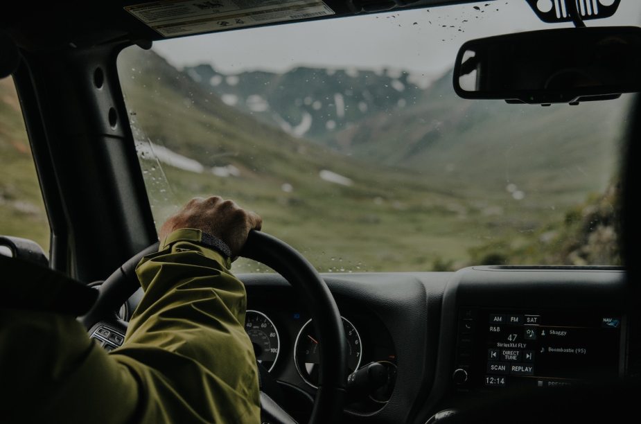 A driver's hands visible on his 4x4's wheel as he navigates driving at high altitude.