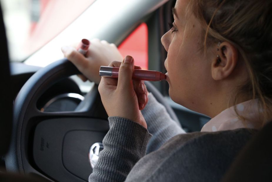 A woman applies lipstick whilst driving.