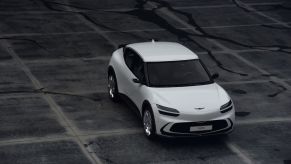 An overhead shot of a white 2023 Genesis GV60 electric SUV model parked on a cracked and stained ground of tiles
