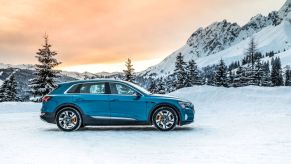 The Audi e-tron all-electric SUV model parked in snow in the mountains as the sun begins to set