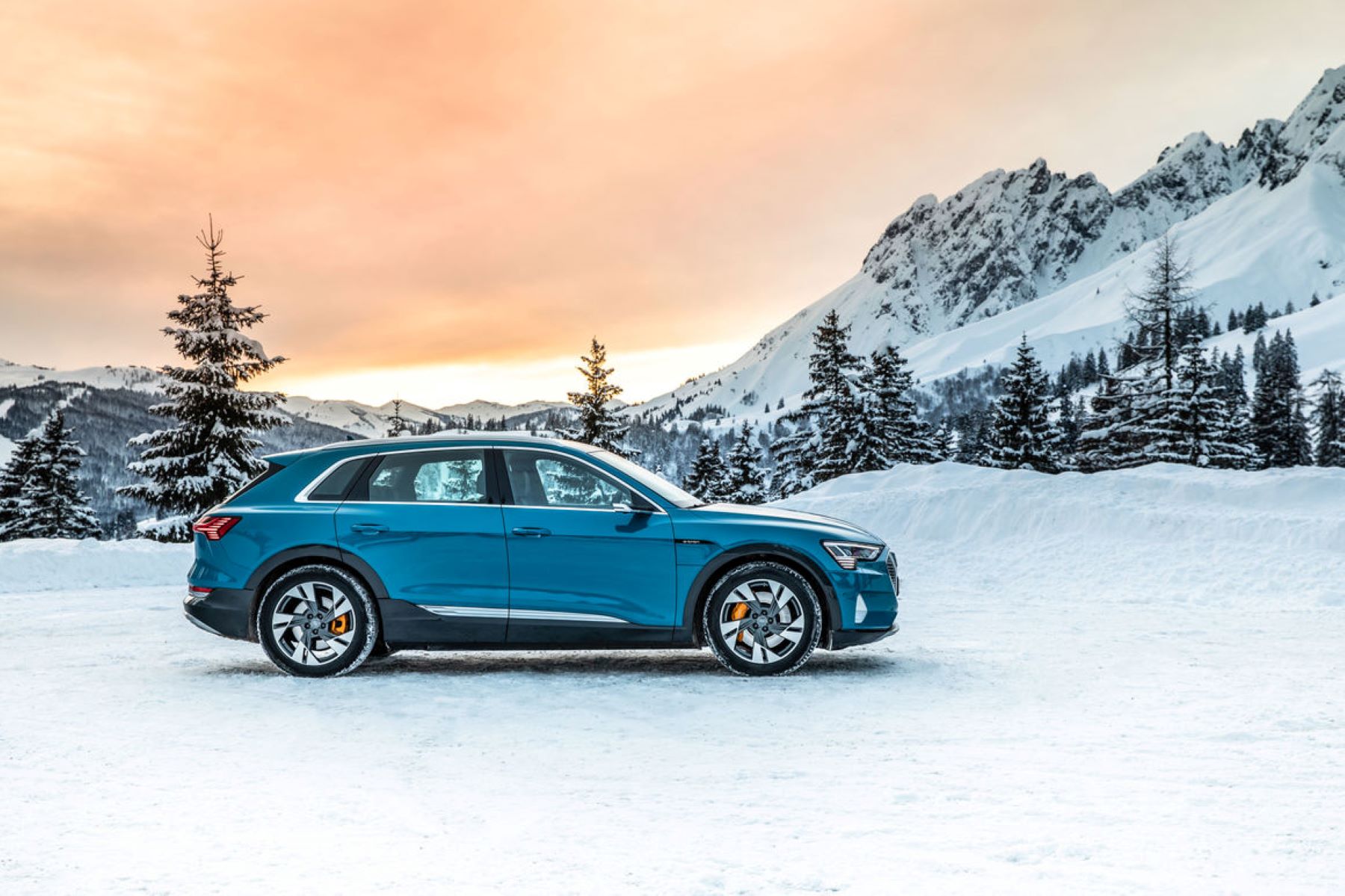 The Audi e-tron all-electric SUV model parked in snow in the mountains as the sun begins to set