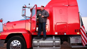 A truck driver standing outside his red semi-truck.