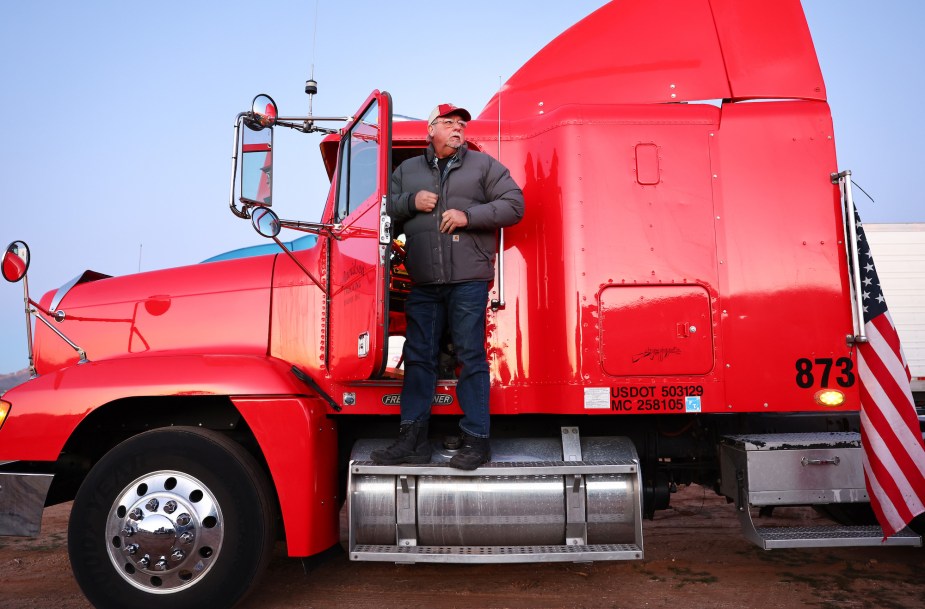 A truck driver standing outside his red semi-truck. 