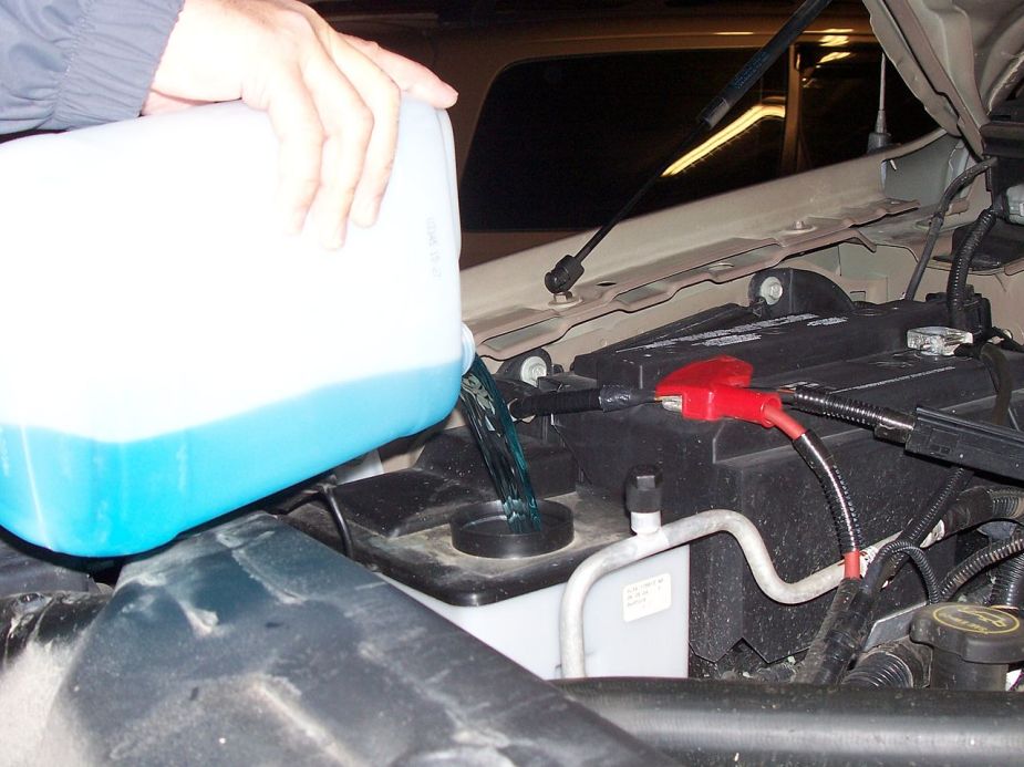 A man pours more washer fluid into a reservoir.