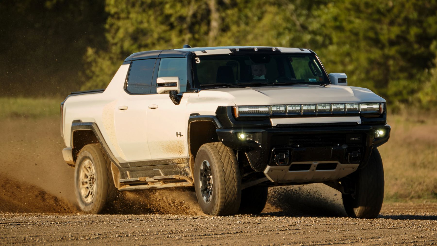 A white GMC Hummer EV electric pickup truck with over 10 inches of ground clearance driving on a dirt field