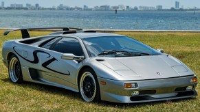 A silver-and-black 1998 Lamborghini Diablo SV on a lawn by a body of water