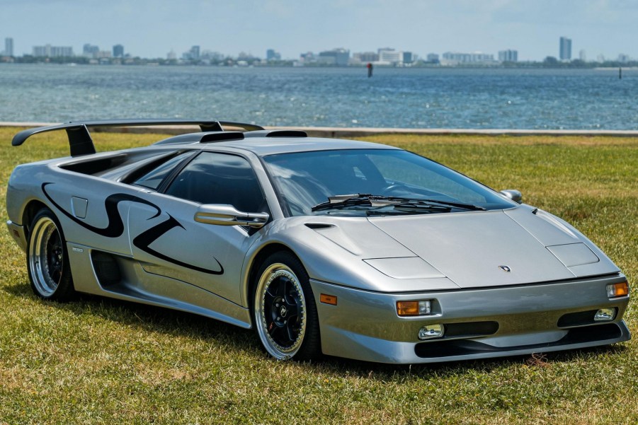 A silver-and-black 1998 Lamborghini Diablo SV on a lawn by a body of water