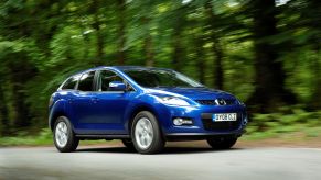 A blue 2008 Mazda CX-7 midsize crossover SUV driving on a forest road